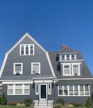 The front of 362 Ives Street, a grey shingled house with a gambrel roof, under a blue sky.