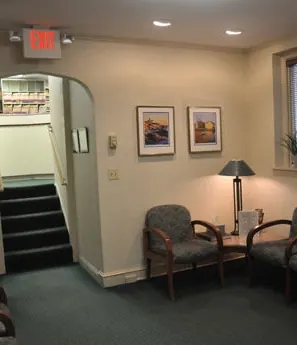 The waiting room by the stairs, with armchairs and framed prints.